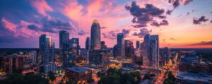 Sunset over a modern city skyline with tall glass skyscrapers and streets glowing with lights.