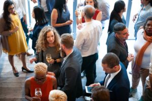 Group of diverse adults at a social mixer, talking and holding wine glasses in a bright venue.