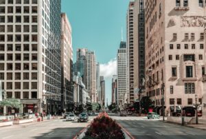City street flanked by tall office buildings, with a landscaped median and cars moving in both directions.