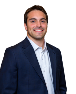 Professional headshot of a smiling man in a navy suit and white shirt against a white background.