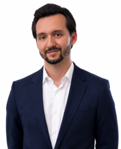 Professional man in a navy suit and white shirt, smiling against a white background, suitable for a corporate headshot.