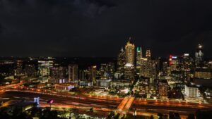 Nighttime city skyline with illuminated skyscrapers and a busy freeway in the foreground.