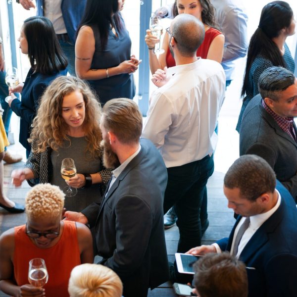 Group of diverse adults at a social mixer, talking and holding wine glasses in a bright venue.