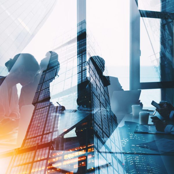 Team of professionals collaborating with laptops and notebooks, overlaid by a city skyline reflection.”