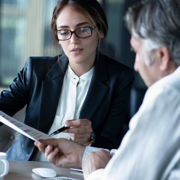 Businesswoman in a blazer and glasses reviews a document with a male colleague at a conference table.
