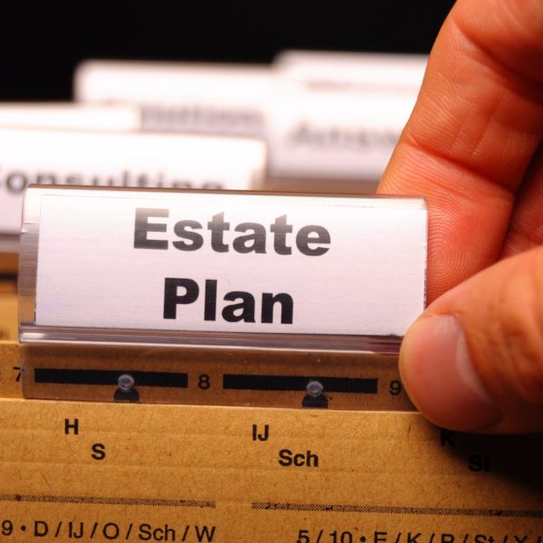 Close-up of a hand placing a label that reads Estate Plan on a filing surface, conveying planning or legal documents.