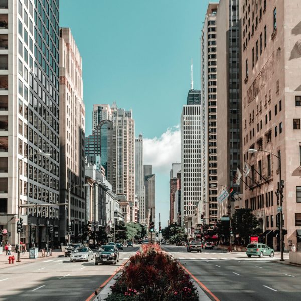 City street flanked by tall office buildings, with a landscaped median and cars moving in both directions.